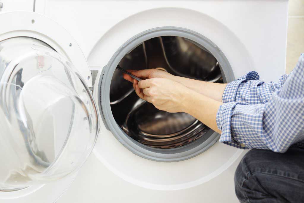 Technician kneels to repair a dryer